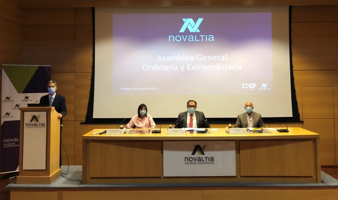 La imagen muestra la Asamblea General Ordinaria y Extraordinaria de Novaltia, celebrada en Zaragoza, donde la cooperativa presentó los resultados del ejercicio 2019. En la mesa presidencial aparecen varios responsables de la entidad, todos con mascarilla, reflejando las medidas sanitarias del momento. Al fondo se proyecta la presentación oficial del acto con el logotipo de Novaltia, mientras un ponente interviene desde el atril. La escena transmite formalidad, transparencia y el compromiso de la cooperativa con la información a sus socios en un año marcado por dificultades y la puesta en marcha de nuevos proyectos e iniciativas de digitalización para las farmacias.