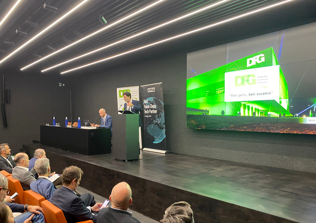Juan Piera interviene en la jornada Move Healthcare 2023, presentada por DFG y Novaltia, ante expertos internacionales en logística farmacéutica, con la imagen del nuevo almacén de DFG proyectada en pantalla.
