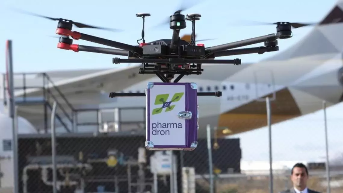Drone del proyecto Pharmadron realizando una prueba de transporte de medicamentos a farmacias, con un contenedor farmacéutico suspendido, en instalaciones aeroportuarias.